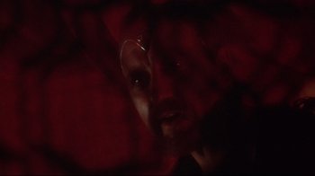 Movie still from “Excalibur” (1981), directed by John Boorman – A man with a beard and glasses in a dark room; Close Up shot, Over the shoulder angle