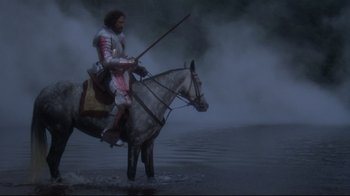 Movie still from “Excalibur” (1981), directed by John Boorman – A man on a horse in a body of water; Wide shot, High angle