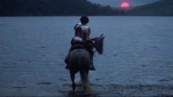 Movie still from “Excalibur” (1981), directed by John Boorman – A man riding a horse through the water at dusk; Extreme Wide shot, Over the shoulder angle