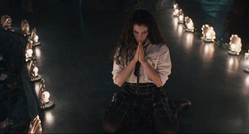 Movie still from “Exotica” (1994), directed by Atom Egoyan – A woman in a white shirt and a black and white plaid skirt praying; Medium shot, High angle