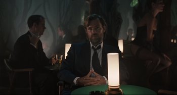 Movie still from “Exotica” (1994), directed by Atom Egoyan – A man sitting at a table in front of a lamp; Medium shot, Over the shoulder angle