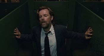 Movie still from “Exotica” (1994), directed by Atom Egoyan – A man in a suit and tie standing in front of a door; Medium shot, Overhead angle