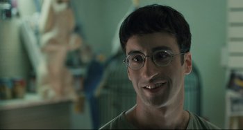 Movie still from “Exotica” (1994), directed by Atom Egoyan – A person wearing glasses and smiling; Close Up shot, Over the shoulder angle