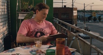 Movie still from “Exotica” (1994), directed by Atom Egoyan – A man sitting at an outdoor table reading a book; Medium shot, Low angle