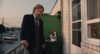 Movie still from “Exotica” (1994), directed by Atom Egoyan – A man in a suit and tie standing in front of a building; Medium shot, Low angle