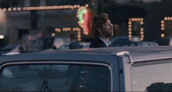 Movie still from “Exotica” (1994), directed by Atom Egoyan – A man in a suit is sitting in the back of a car; Medium shot, Over the shoulder angle