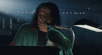 Movie still from “Exotica” (1994), directed by Atom Egoyan – A person sitting at a microphone with a parrot; Close Up shot, Low angle