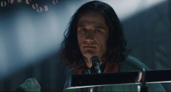 Movie still from “Exotica” (1994), directed by Atom Egoyan – A man with long black hair standing at a podium; Close Up shot, Low angle