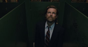 Movie still from “Exotica” (1994), directed by Atom Egoyan – A man wearing a suit and tie standing in front of a door; Medium shot, Low angle