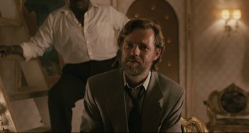 Movie still from “Exotica” (1994), directed by Atom Egoyan – A man in a suit and tie sitting in front of another man in a suit; Medium shot, Over the shoulder angle