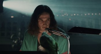 Movie still from “Exotica” (1994), directed by Atom Egoyan – A man with long black hair is holding a microphone; Close Up shot, Over the shoulder angle