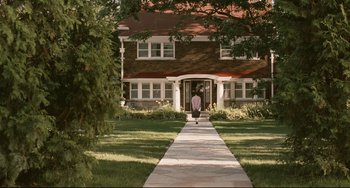 Movie still from “Exotica” (1994), directed by Atom Egoyan – A person walking down a sidewalk in front of a house; Extreme Wide shot, Over the shoulder angle