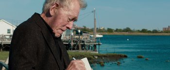 Movie still from “Extremely Loud & Incredibly Close” (2011), directed by Stephen Daldry – An older man writing on a piece of paper near a body of water; Close Up shot, Over the shoulder angle