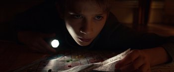 Movie still from “Extremely Loud & Incredibly Close” (2011), directed by Stephen Daldry – A young boy is reading a book in the dark with a flashlight; Close Up shot, High angle