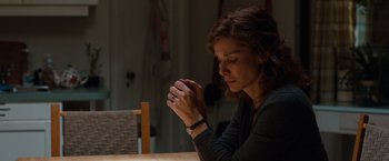Movie still from “Extremely Loud & Incredibly Close” (2011), directed by Stephen Daldry – A woman sitting at a table with her hands clasped together; Close Up shot, Over the shoulder angle