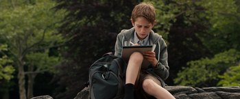 Movie still from “Extremely Loud & Incredibly Close” (2011), directed by Stephen Daldry – A boy sitting on the ground using a tablet computer; Medium shot, Over the shoulder angle