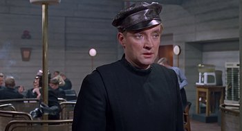 Movie still from “Fahrenheit 451” (1966), directed by François Truffaut – A man wearing a hat in a room with other people; Close Up shot, Over the shoulder angle