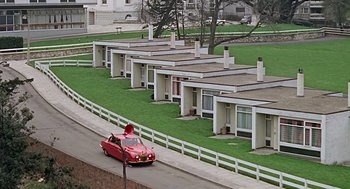 Movie still from “Fahrenheit 451” (1966), directed by François Truffaut – A red car parked on the side of the road near some houses; Extreme Wide shot, High angle
