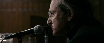 Movie still from “Fair Game” (2010), directed by Doug Liman – An older man with glasses is speaking into a microphone; Close Up shot, Over the shoulder angle