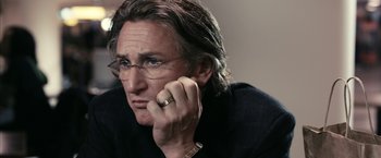 Movie still from “Fair Game” (2010), directed by Doug Liman – A person wearing glasses and holding a cell phone to his ear; Close Up shot, Over the shoulder angle