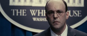 Movie still from “Fair Game” (2010), directed by Doug Liman – A man in a suit and tie standing in front of a building; Close Up shot, Over the shoulder angle