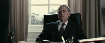 Movie still from “Fair Game” (2010), directed by Doug Liman – A man in a suit sitting at a desk in front of a window; Close Up shot, Low angle