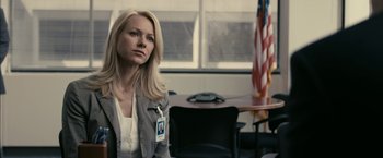 Movie still from “Fair Game” (2010), directed by Doug Liman – A woman with a badge on her chest in an office setting; Medium shot, Over the shoulder angle