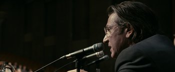 Movie still from “Fair Game” (2010), directed by Doug Liman – A man with glasses is speaking into a microphone; Close Up shot, Low angle