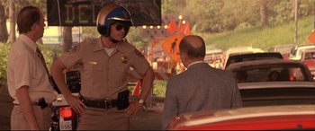 Movie still from “Falling Down” (1993), directed by Joel Schumacher – A man in a suit and helmet talking to a police officer; Medium shot, Over the shoulder angle