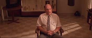 Movie still from “Falling Down” (1993), directed by Joel Schumacher – A man sitting in a chair wearing a shirt and tie; Medium shot, Low angle
