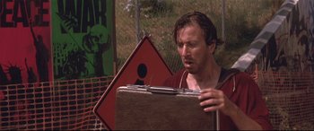 Movie still from “Falling Down” (1993), directed by Joel Schumacher – A man holding a briefcase while standing next to a road sign; Close Up shot, Low angle