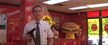 Movie still from “Falling Down” (1993), directed by Joel Schumacher – A man standing in front of a giant hamburger in a room; Medium shot, Low angle
