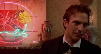 Movie still from “Fandango” (1985), directed by Kevin Reynolds – A man wearing a suit and tie in front of a neon sign; Close Up shot, Over the shoulder angle