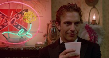 Movie still from “Fandango” (1985), directed by Kevin Reynolds – A man in a suit holding a cup in his hand; Close Up shot, Over the shoulder angle