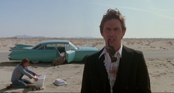 Movie still from “Fandango” (1985), directed by Kevin Reynolds – A man standing in front of an abandoned car; Medium shot, Low angle