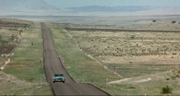 Movie still from “Fandango” (1985), directed by Kevin Reynolds – A car driving down the middle of a road; Extreme Wide shot, High angle