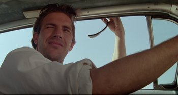Movie still from “Fandango” (1985), directed by Kevin Reynolds – A person in a car holding a spoon; Close Up shot, Low angle