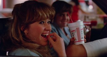 Movie still from “Fandango” (1985), directed by Kevin Reynolds – A woman eating a soft drink while sitting next to another woman; Close Up shot, Over the shoulder angle