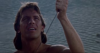 Movie still from “Fandango” (1985), directed by Kevin Reynolds – A shirtless man holding a fishing pole in front of a body of water; Close Up shot, Low angle