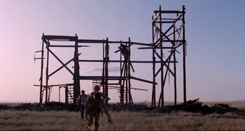 Movie still from “Fandango” (1985), directed by Kevin Reynolds – A group of people walking in a field near some wooden structures; Extreme Wide shot, Low angle
