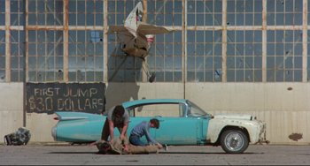 Movie still from “Fandango” (1985), directed by Kevin Reynolds – Two men working on a car on the side of the road; Wide shot, Low angle