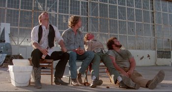 Movie still from “Fandango” (1985), directed by Kevin Reynolds – A group of men sitting on top of a wooden bench; Wide shot, Low angle