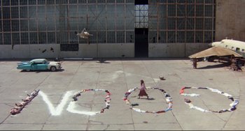 Movie still from “Fandango” (1985), directed by Kevin Reynolds – A girl is sitting on the ground in front of a skateboard park; Extreme Wide shot, Overhead angle