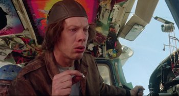 Movie still from “Fandango” (1985), directed by Kevin Reynolds – A man in a brown jacket and a brown hat is holding a red object; Close Up shot, Low angle