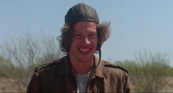 Movie still from “Fandango” (1985), directed by Kevin Reynolds – A man wearing a hat and a brown jacket smiling; Close Up shot, Low angle