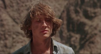 Movie still from “Fandango” (1985), directed by Kevin Reynolds – A young man with long hair and a blue shirt is looking to his left; Close Up shot, Low angle