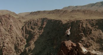 Movie still from “Fandango” (1985), directed by Kevin Reynolds – A man standing on top of a mountain holding up his hand; Extreme Wide shot, Low angle