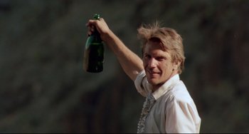 Movie still from “Fandango” (1985), directed by Kevin Reynolds – A man holding up a bottle of champagne; Close Up shot, Low angle