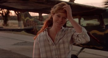 Movie still from “Fandango” (1985), directed by Kevin Reynolds – A woman standing in front of an airplane with her hand on her head; Close Up shot, Over the shoulder angle