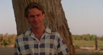 Movie still from “Fandango” (1985), directed by Kevin Reynolds – A man standing next to a tree smiling for the camera; Close Up shot, Low angle